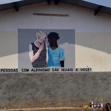 Flavia Pinto, head of Azemap, a volunteer-run organization that supports people with albinism, stands before a mural painted at a school in Tete province. The mural reads: "People with albinism are the same as you!"