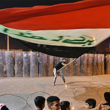 A protester waves an Iraqi flag while security forces hold a line opposite anti-government protesters in Basra, Iraq on Wednesday, Nov 4, 2020.