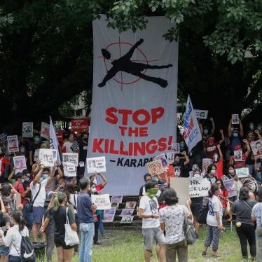 Protesters hold signs during a rally in front of a giant banner that reads, "Stop The Killings."