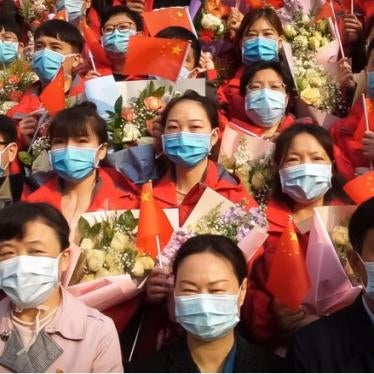 Image of people wearing face masks and holding Chinese flags and brightly-colored flowers.