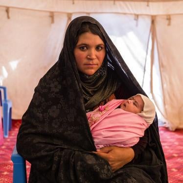 A woman holding a baby poses for the camera inside a large tent