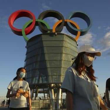 Personas con máscaras delante de una escultura de los anillos olímpicos