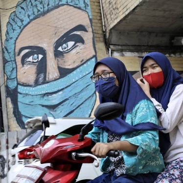 Women ride a motorbike past a large Covid-19-themed mural in Jakarta, Indonesia, October 2, 2020.