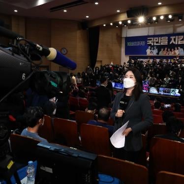 A woman in a face mask holds a microphone in front of a video camera