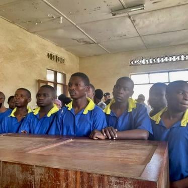 A group of men in prison uniforms stand in a court room 