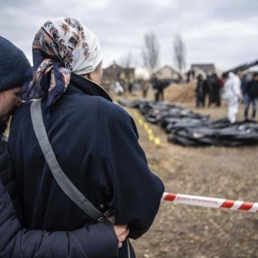 Women watch and embrace each other as bodies are exhumed from a mass grave by the authorities