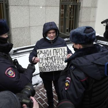 Police officers detain a demonstrator holding a poster reading "Hands off Memorial, freedom for political prisoners"