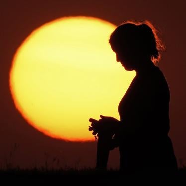 A woman stands in front of a setting sun