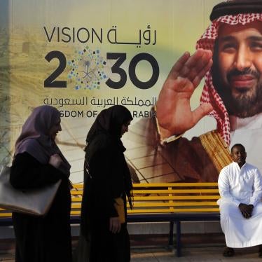 People walk past a Vision 2030 banner showing Saudi Crown Prince Mohammed bin Salman.