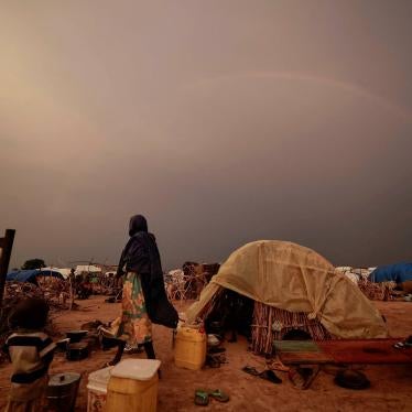 A woman stands by a tent in a refugee camp