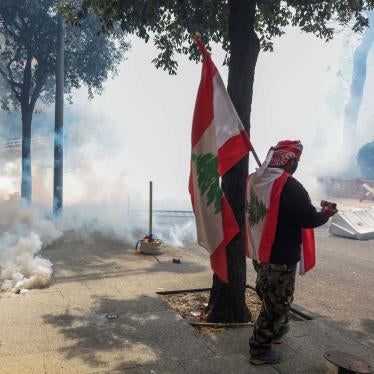 A demonstrator holds a Lebanese flag as he stands near smoke rising from tear gas during a protest over the deteriorating economic situation, at Riad al-Solh square in Beirut, Lebanon.