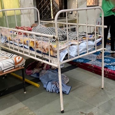 An individual lying in a metal-framed bed inside the Asha Kiran institution.