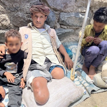 عبد الله (35 عاما) خسر ساقيه جراء لغم أرضي بينما كان يأخذ الماعز للرعي، يجلس على الأرض مع طفليه في الشقب، اليمن في 27 أبريل/نيسان 2024. © 2024 نيكو جعفرنيا/هيومن رايتس ووتش