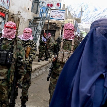 An Afghan woman walks by Taliban security personnel inalong a market in the Baharak district of Badakhshan province, February 26, 2024.