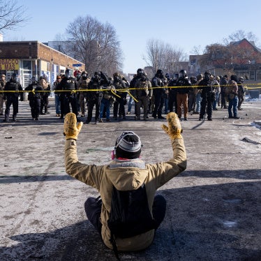 A protester sits on the street with his arms up in front of federal agents and Minneapolis Police