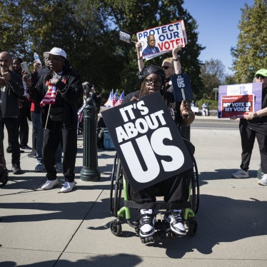 A man in a wheelchair holds a protest sign at a demonstration