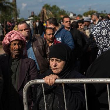 In Tripoli, Lebanon. Syrian Refugees line up to register or renew their registration at the UNHCR compound. A woman stands by a barrier. 