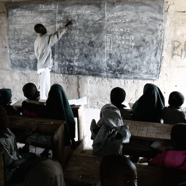 A picture of a teacher writing on a black board while students pay attention.