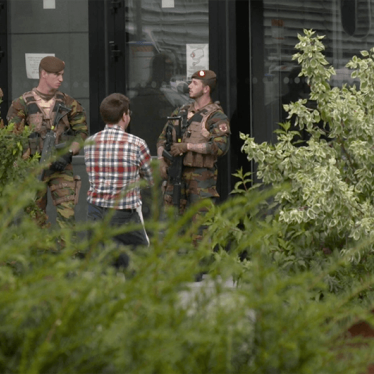 A photo of two Belgian soldiers speaking to a civilian.