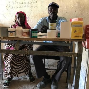 Mukuma Hamad, a volunteer health worker (L), and James Atai, a nurse, sit at a table displaying almost the total stock of basic medicines in the only health clinic in Hadara village, rebel-controlled Southern Kordofan. 