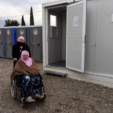 Naima, a 70-year-old woman with a disability from Aleppo, Syria, with her daughter, Hasne, in front of the shower area in Cherso camp, Thessaloniki, Greece. The showers are not accessible for people who use a wheelchair. 