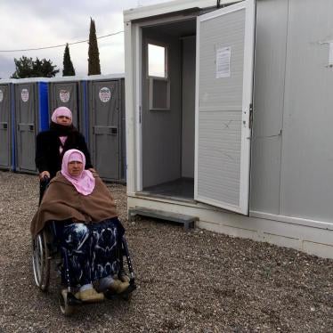 Naima, a 70-year-old woman with a disability from Aleppo, Syria, with her daughter, Hasne, in front of the shower area in Cherso camp, Thessaloniki, Greece. The showers are not accessible for people who use a wheelchair. 