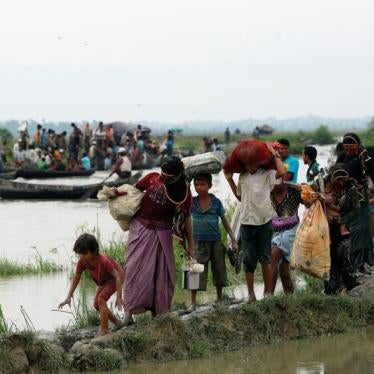 Rohingya refugees walk on a muddy path as others travel on a boat after crossing the Bangladesh-Myanmar border, in Teknaf, Bangladesh, September 6, 2017.