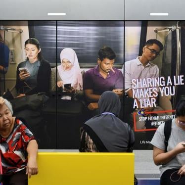 Commuters sit in front of an advertisement discouraging the dissemination of fake news, at a train station in Kuala Lumpur, Malaysia March 28, 2018.