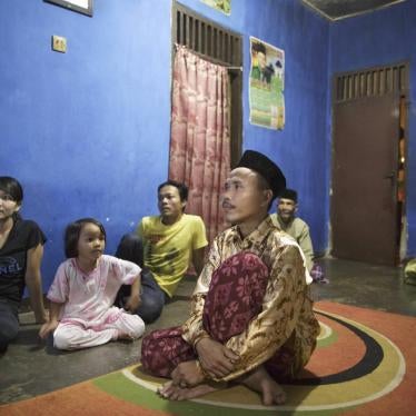Members of a family sit on the floor at home watching tv. 