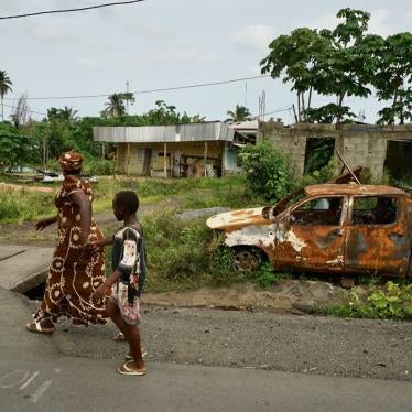 A mother and child walk past a destroyed car in a small town near Buea in southwest Cameroon, May 11, 2019.
