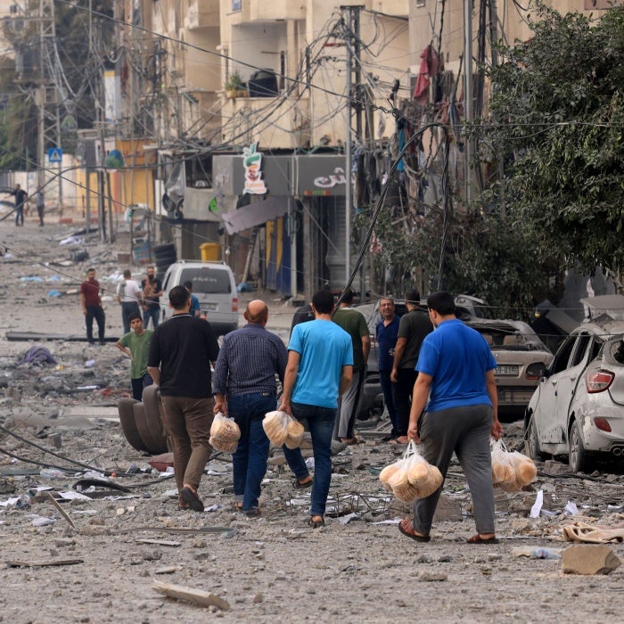  Palestinian men carry bread through a heavily bombed street following Israeli airstrikes on Gaza City on October 10, 2023.  