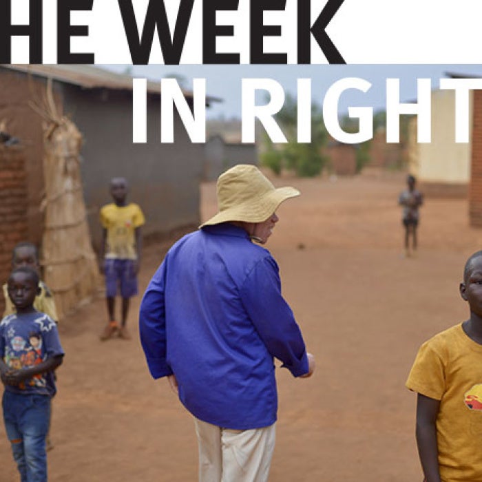 Photo of man in blue shirt and white hat, walking among children in Malawi 